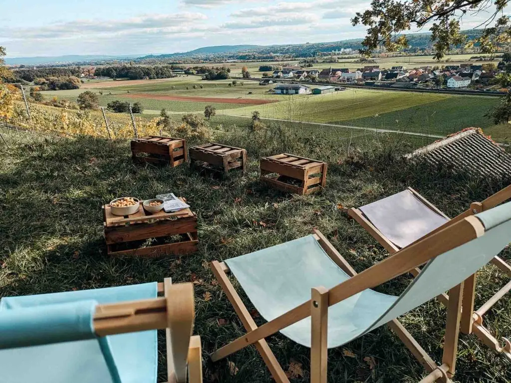 Kleiner Sitzbereich mit Liegestühlen und Holzkisten inmitten des Weinbergs, mit Blick über die Landschaft.