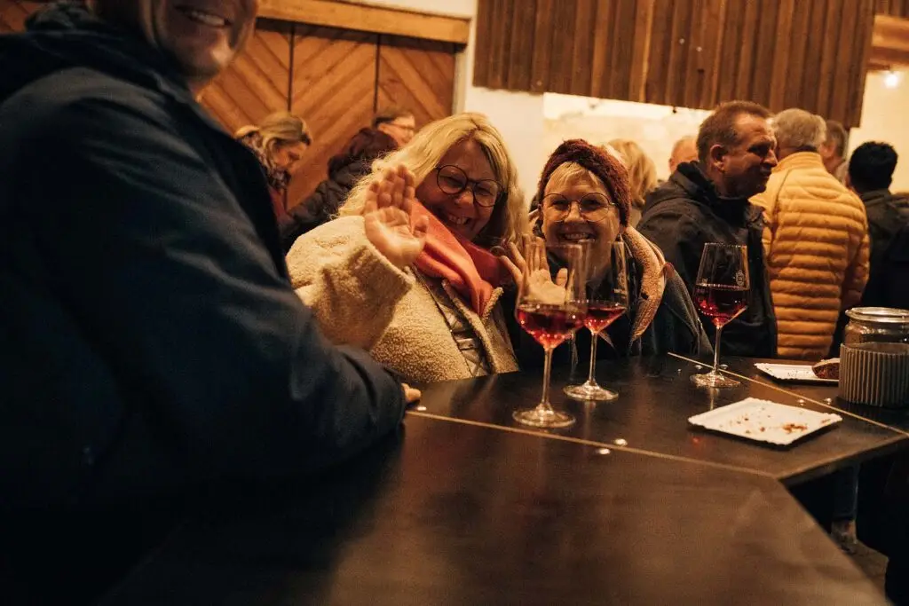Gruppe fröhlicher Gäste mit Rotwein am Stehtisch beim Winterfest 2025 im Weingut Weyrauther